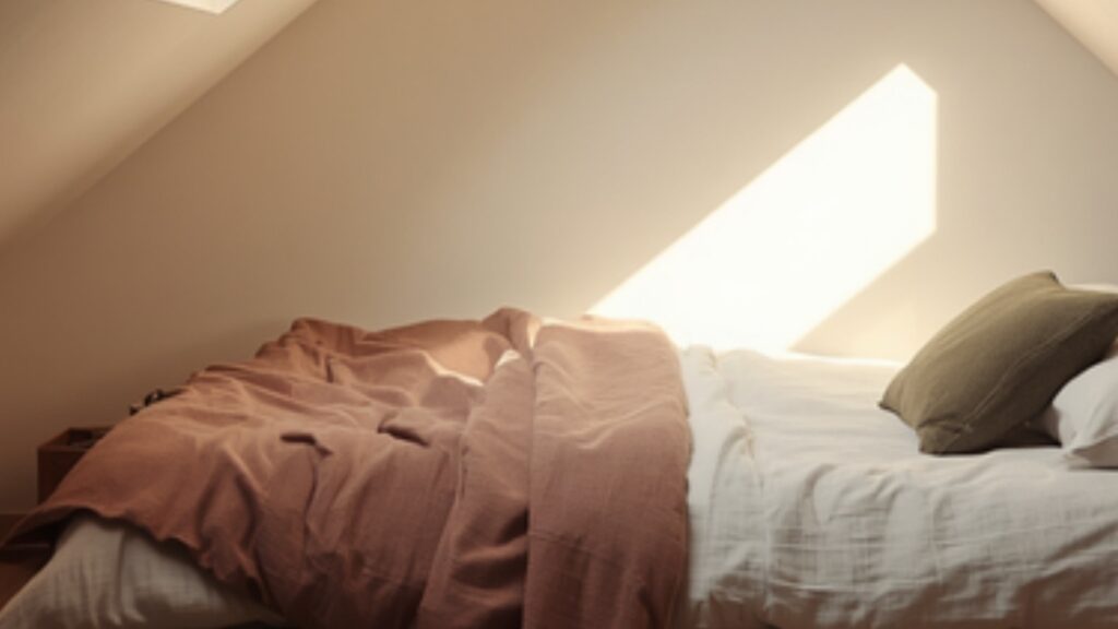 Kleine zolder slaapkamer met schuin dak, laag bed onder de schuine wand met daglicht uit het dakraam